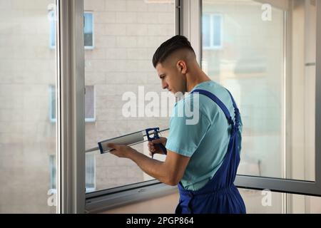 Bauarbeiter versiegelt Fenster mit Versiegelung in Innenräumen Stockfoto