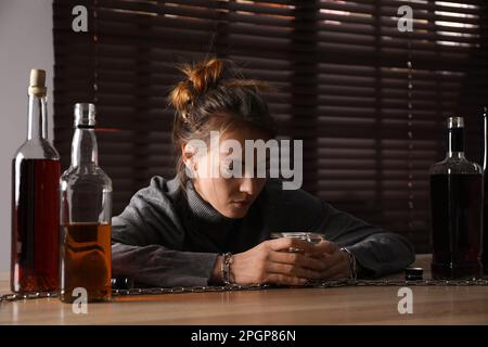 Alkoholsucht. Frau mit einem Glas Schnaps an einem Holztisch im Zimmer angekettet Stockfoto