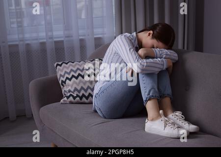 Unglückliche junge Frau auf dem Sofa zu Hause, Platz für Text. Einsamkeitskonzept Stockfoto
