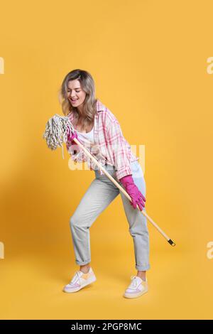 Wunderschöne junge Frau mit Mopp, der auf orangefarbenem Hintergrund singt Stockfoto