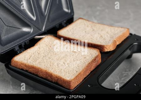 Moderner Sandwichautomat mit Brotscheiben auf grauem Tisch, Nahaufnahme Stockfoto