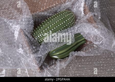 Keramikkakti mit Luftpolsterfolie in Karton auf Holztisch, Draufsicht Stockfoto