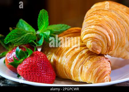 Wunderschönes, schickes Video auf weißem Teller zwei Croissants, riesige Erdbeeren- und Minzbonbons, die die Kamera langsam zurückziehen und ein köstliches französisches Frühstücksrestaurant Filmen, das frisches Gebäck serviert, unglaublich schick Stockfoto