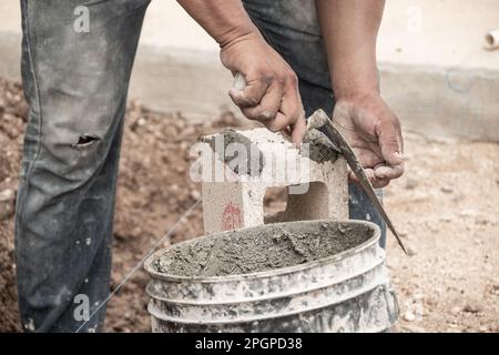 Die Hände eines Arbeiters, der Zement auf einen Spachtel legt Stockfoto