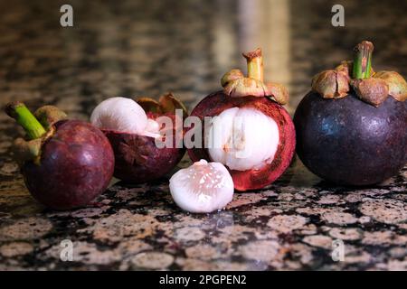 Mangosteen bereit, Früchte von Thailand zu essen, selektive Fokus asiatische thailändische Mangostanfrüchte stehen auf einem Marmortisch in einem Abschnitt einige Stücke schwarze tropische Früchte Hintergrund Stockfoto