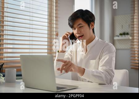 Erfolgreicher und professioneller asiatischer Millennials-Geschäftsmann oder männlicher Manager, der ein formelles Telefongespräch mit seinem Geschäftspartner führt, um einige Details zu erfahren Stockfoto