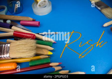 Overhead-Aufnahme von Schulmaterial mit Risikotext. Pinsel, Bleistifte, künstlerische Werkzeuge. Kunst- Und Handwerksgeräte. Stockfoto