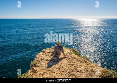 Der Marinha Beach an der Algarve, Portugal, ist das Rückgrat einer jungen Frau, die auf den Klippen sitzt und in die Schönheit des Atlantischen Ozeans eintaucht Stockfoto