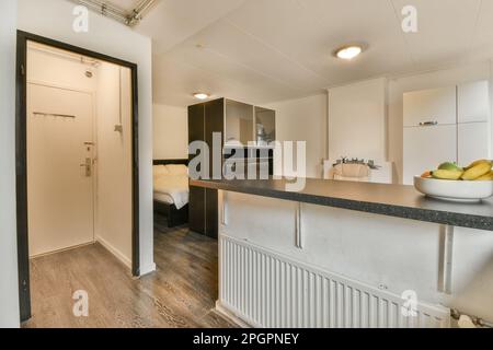 Eine Küche und Essbereich in einem winzigen Apartment mit weißen Wänden, Holzboden und einer offenen Tür, die zum Wohnzimmer führt Stockfoto