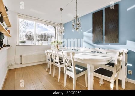Ein Speisesaal mit blauen Wänden und Hartholzfußboden, einschließlich eines weißen runden Tisches umgeben von vier Holzstühlen Stockfoto