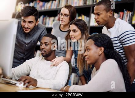 Haben sich darauf konzentriert, die bestmöglichen Ergebnisse zu erzielen. Eine Gruppe junger Studenten, die einen Computer zusammen in einer Collegebibliothek benutzen. Stockfoto
