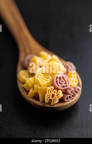 Pasta in verschiedenen unheimlichen Formen. Ungekochte halloween-Pasta in Löffel auf einem schwarzen Tisch. Stockfoto