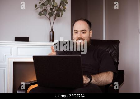 Der Mann arbeitet bequem von zu Hause aus und hält seinen Laptop in der Hand. Gesichtsausdruck der Fernarbeit Stockfoto