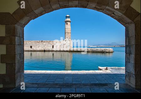 Historischer Leuchtturm Rethymon, eingerahmt von einem der Gebäude am Hafen, Rethymno, Kreta, Griechenland. Stockfoto