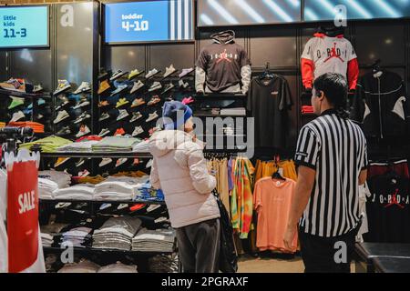 In den großen Fenstern des Geschäfts ist eine Reihe von Sportschuhen und Bekleidung zu sehen, während Kunden Schuhe kaufen. Foot locker, der in den USA ansässige Schuhhändler, durchläuft derzeit in Asien einen Wandel, da es sein Geschäftsmodell vereinfachen und sich auf Kernregionen und Banner konzentrieren will. In diesem Rahmen wird Foot locker sowohl seine eCommerce- als auch seine Ladengeschäfte in Hongkong und Macau schließen und gleichzeitig alle seine derzeitigen eigenen und selbstbetriebenen Ladengeschäfte und eCommerce in Singapur und Malaysia auf ein Lizenzmodell umstellen. Die Ergebnisse von Foot locker für das vierte Quartal 2022 zeigten, dass das Unternehmen eine Serie macht Stockfoto