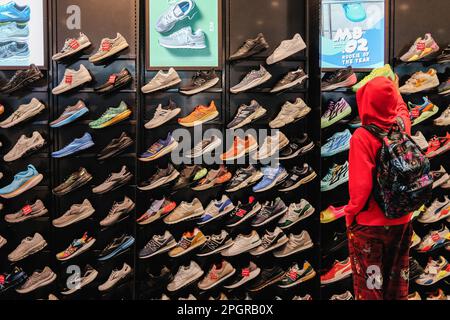 In den großen Fenstern des Geschäfts ist eine Reihe von Sportschuhen und Bekleidung zu sehen, während Kunden Schuhe kaufen. Foot locker, der in den USA ansässige Schuhhändler, durchläuft derzeit in Asien einen Wandel, da es sein Geschäftsmodell vereinfachen und sich auf Kernregionen und Banner konzentrieren will. In diesem Rahmen wird Foot locker sowohl seine eCommerce- als auch seine Ladengeschäfte in Hongkong und Macau schließen und gleichzeitig alle seine derzeitigen eigenen und selbstbetriebenen Ladengeschäfte und eCommerce in Singapur und Malaysia auf ein Lizenzmodell umstellen. Die Ergebnisse von Foot locker für das vierte Quartal 2022 zeigten, dass das Unternehmen eine Serie macht Stockfoto