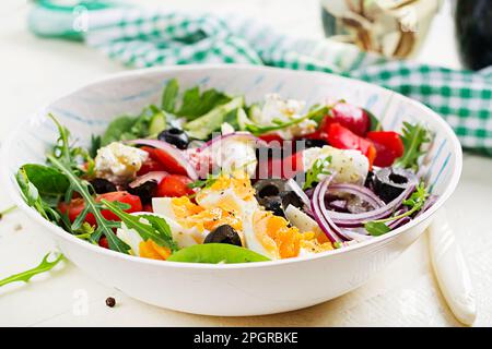 Frühstück. Griechischer Salat und gekochte Eier. Frischer Gemüsesalat mit Tomaten, Gurken, Oliven, Rucola und Frischkäse. Trendiges Essen. Stockfoto