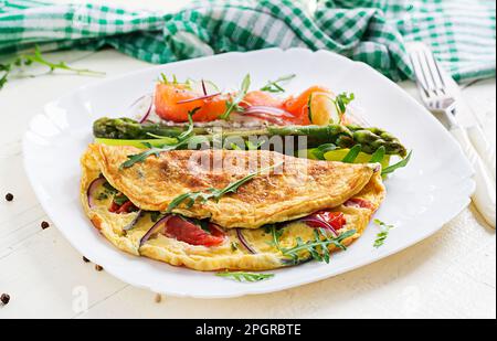 Ketogenes Frühstück. Omelette mit Tomaten, roten Zwiebeln, Sandwich mit Lachs und geröstetem Spargel. Italienische Frittata. Keto, ketogenes Mittagessen. Stockfoto