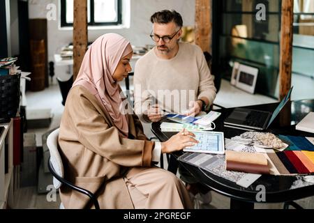 Zwei multinationale Kollegen, die in einer gemütlichen Werkstatt an Computern arbeiten Stockfoto