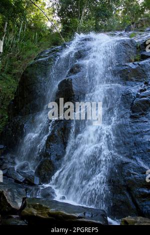 Nahaufnahme des Nakalitkalit Wasserfalls in El Nido, Palawan auf den Philippinen, der über schwarze Felsen fließt, umgeben von Regenwald. Stockfoto