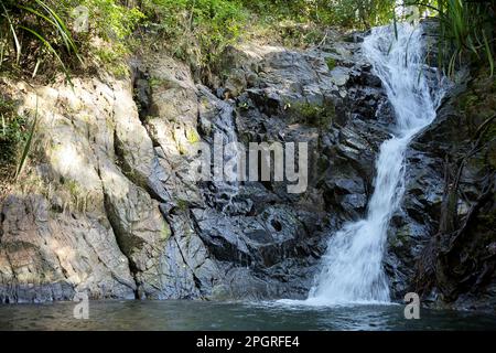 Nahaufnahme des Nakalitkalit-Wasserfalls in El Nido, Palawan auf den Philippinen, der über schwarze Felsen in ein von Regenwald umgebenes Wasserbecken fließt. Stockfoto