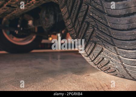 Niedrige Sicht auf ein Auto und seine Reifen in der Reparaturwerkstatt. Konzept des PKW-Wartungsdienstes. Speicherplatz kopieren. Stockfoto
