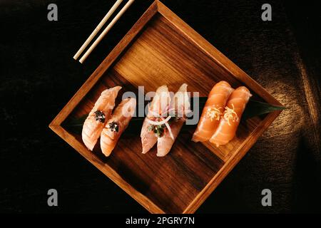 Eine hölzerne Platte mit verschiedenen Sushi-Stücken, begleitet von einem Paar Essstäbchen, auf weißem Hintergrund Stockfoto