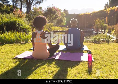 Rückansicht eines afroamerikanischen Seniorenpaares, das im sonnigen Garten Yoga auf Matte trainiert. Zu Hause in Isolation bleiben während Quarantäne-Abriegelung Stockfoto