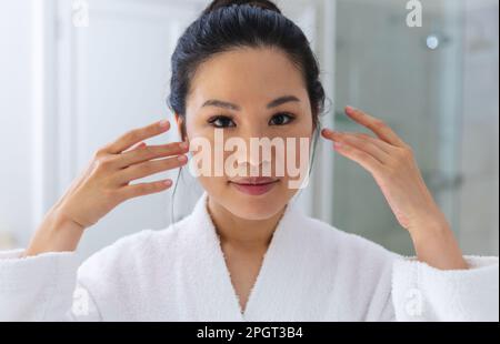 Porträt einer glücklichen Asiatin, die einen Bademantel trägt und in den Badezimmerspiegel schaut. Lifestyle, Selbsthilfe, Gesundheit und Schönheit. Stockfoto