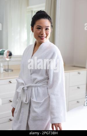 Porträt einer glücklichen asiatischen Frau, die im Bad lächelnd im Bademantel sitzt. Lifestyle, Selbsthilfe, Gesundheit und Schönheit. Stockfoto