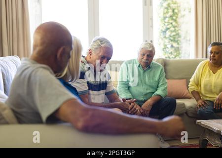 Eine Gruppe verschiedener Senior-Freunde, die im Wohnzimmer sitzen, sich unterhalten und sich gegenseitig aufheitern. Ruhestand, Freundschaft und Unterstützung. Stockfoto