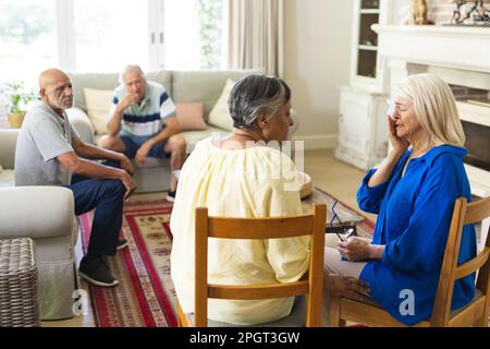 Eine Gruppe verschiedener Senior-Freunde, die im Wohnzimmer sitzen und sich während der Gruppentherapie unterhalten. Seniorenleben, Freundschaft und Unterstützung. Stockfoto