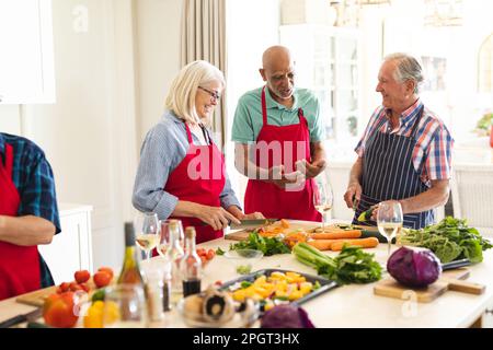 Glückliche Gruppe von verschiedenen Senior-Freunden in Schürzen, die sich während des Kochkurses unterhielten. Ruhestand, Lernen, Kochen und gesunder Lebensstil. Stockfoto