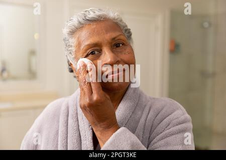 Nahaufnahme einer afroamerikanischen Seniorin im Bademantel, die zu Hause ihr Gesicht mit Baumwolle abwischte. Unverfälscht, Körperpflege, Altern, Verwöhnung, Porträt, Schönheit Stockfoto