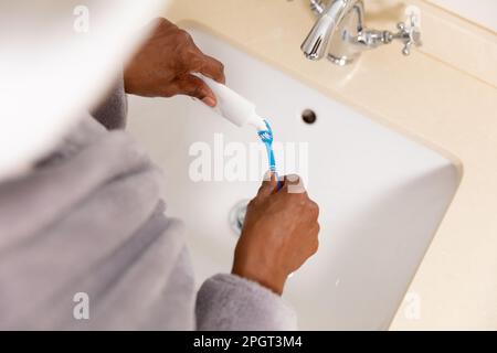 Gekürzte Hände einer afroamerikanischen Seniorin, die Zahnpasta auf die Zahnbürste über das Waschbecken aufträgt. Kopierraum, unverändertes, Lebensstil, Zahnhygiene, Stockfoto