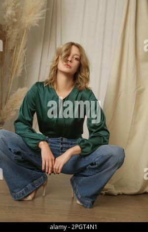 Studiofotos eines jungen weiblichen Models in kiefergrüner Seidenbluse und legeren Jeans Stockfoto