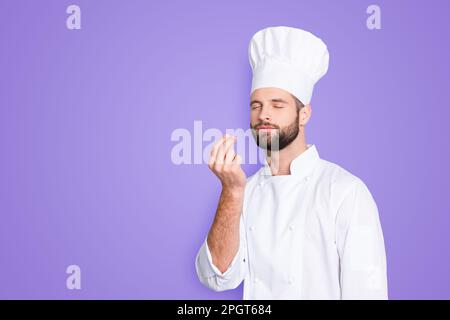 Porträt mit Kopierraum, leerer Platz für Werbung, Produkt eines attraktiven Kochs in Baskenmütze mit geschlossenen Augen, weißes Outfit, das Bellisimo-Symbol macht Stockfoto