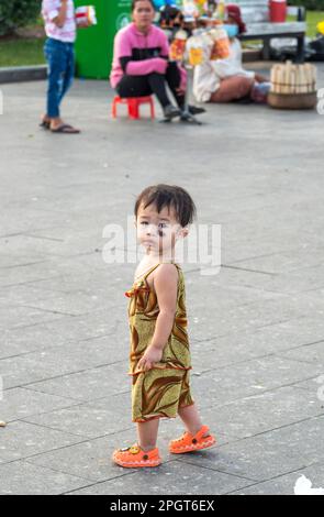 Phnom Penh, Kambodscha-Dezember 23. 2022: Ein kleiner Junge, der kleine Sohn von lokalen Straßenhändlern, schaukelt herum, während seine Mutter am Sisowath Quay, im ansieht Stockfoto