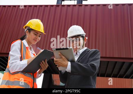 Lagerbetriebsleiter und Hafenarbeiter, die Container nach dem Verladen im Handelshafen bearbeiten und überprüfen. Logistik, Transport, Import und Export Stockfoto