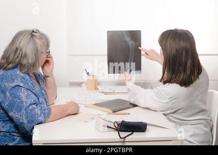 Junge Ärztin zeigt ihrem älteren Patienten ein Röntgenbild Stockfoto