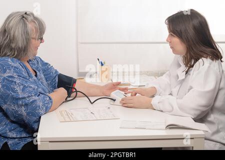 Junge Ärztin, die den Blutdruck ihrer älteren Patientin in der Praxis misst Stockfoto