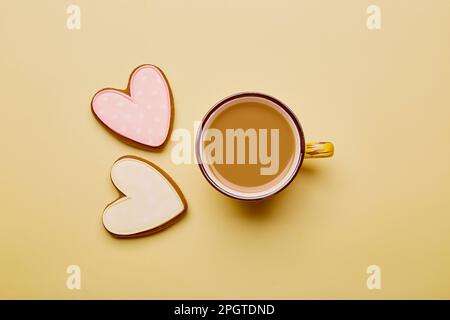 Ästhetische Kaffeetasse und geformte Herzkekse. Frühlingskarte mit gebackenen, glasierten Keksen auf gelbem Hintergrund. Frühstück, weibliches Konzept. Frauentag, Mo Stockfoto