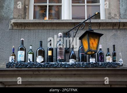 Zürich, Schweiz - 21. Februar 2023: Verschiedene Flaschen an der Fassade eines alten Hauses neben einer beleuchteten Lampe Stockfoto