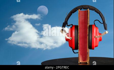 Hörbuch und Oldtimer-Kopfhörer vorne, Himmelshintergrund, Wolke und aufsteigender Mond. Stockfoto