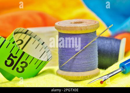 Nähwerkzeuge auf farbige Kleidung mit Makrodetails wie Fadenrollen, Nadel, Maßband und Gewindespflücker. Stockfoto