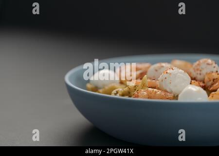 Penne-Pasta mit Garnelen und Mozzarella und Pesto in blauer Schale mit Kopierfläche, flacher Fokus Stockfoto