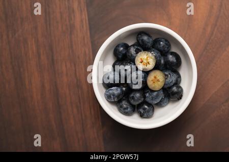 Blick von oben auf reife Heidelbeeren in einer weißen Schüssel auf Holztisch, von oben nach unten Stockfoto