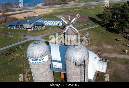 Alt Schwerin, Deutschland. 24. März 2023. Die historische Windmühle und Getreidesilos aus der DDR-Zeit befinden sich auf dem Gelände der Agrargeschichte Agroneum. Das Landwirtschaftsmuseum ist ein Freiluftmuseum und öffnet seine Türen für interessierte Besucher an Wochenenden nach den Winterferien. Die Agrargeschichte von Mecklenburg zeigt sich hier von der Mitte des 19. Jahrhunderts bis heute. (Luftaufnahme mit Drohne) Kredit: Jens Büttner/dpa/Alamy Live News Stockfoto