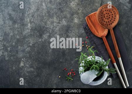 Frischer Rosmarin und Safran in Marmormörtel und Holzlöffel auf schwarzem Steinhintergrund. Hintergrund der Kochkunst. Zutaten zum Kochen von Backgr Stockfoto