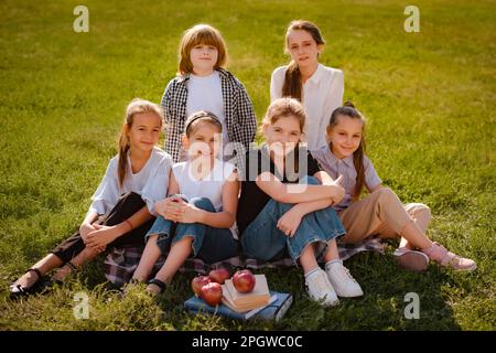 Glückliche Kinder, die auf grünem Gras sitzen und lächeln. Fröhliche Kinder verbringen Zeit im Sommercamp, finden neue Freunde und spielen draußen. Gruppenporträt Stockfoto